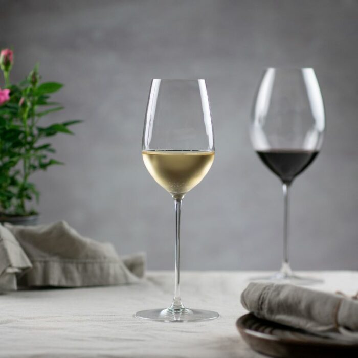 Et vinglass med hvitvin og et med rødvin, ved siden av blomst og tøyserviett
